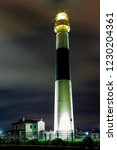 Time exposure of tall illuminated black and white banded lighthouse lighting sky at night