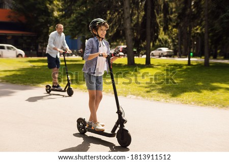Time With Family. Laughing son using motorized kick scooter with his dad on a sunny day, copy space