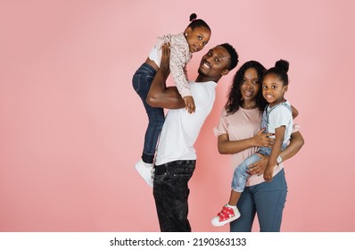 Time With Family. Overjoyed African American Family Laughing And Posing Isolated Over Pink Studio Wall. Cheerful Father And Mom Carrying Their Daughters On Hands.