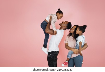 Time With Family. Overjoyed African American Family Laughing And Posing Isolated Over Pink Studio Wall. Cheerful Father And Mom Carrying Their Daughters On Hands.