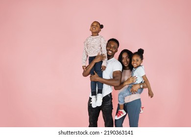 Time With Family. Overjoyed African American Family Laughing And Posing Isolated Over Pink Studio Wall. Cheerful Father And Mom Carrying Their Daughters On Hands.