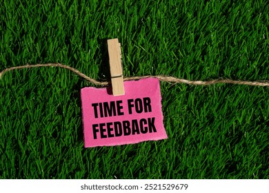 Time for feedback message written on ripped torn pink paper piece with green grass background. Conceptual time for feedback symbol. Copy space.