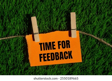 Time for feedback message written on ripped torn orange paper piece with green grass background. Conceptual time for feedback symbol. Copy space.