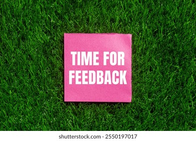 Time for feedback message written on ripped torn pink paper with green grass background. Conceptual time for feedback symbol. Copy space.