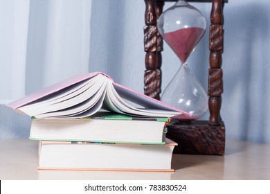 Time (for Studying Or Working) Is Running Out. A Giant Handmade Wooden Hourglass Or Sand Clock With Pink Sand Next To A Stack Of Three Thick Colorful School Books.