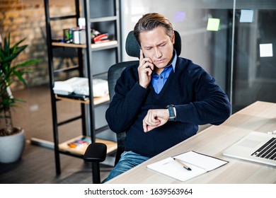 It is time. Handsome businessman checking time while talking per telephone