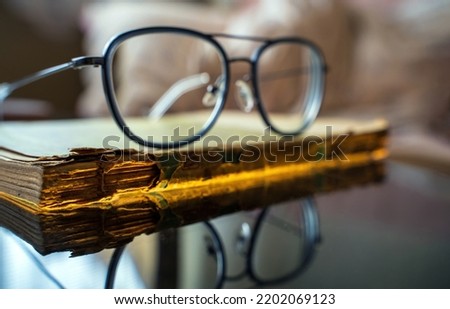 Time and knowledge concept, An eye glasses or spectacles kept on top of a really old torn and partially damaged religious scripture book. Extreme macro close up shot of an old vintage book.