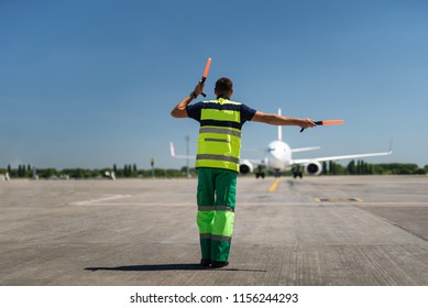 Time for landing. Aviation marshaller meeting passenger plane at the airport