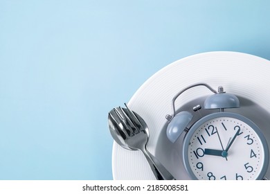 Time to lose weight , intermittent fasting eating control or time to diet concept , alarm clock with dish and spoon  decoration on blue background - Shutterstock ID 2185008581
