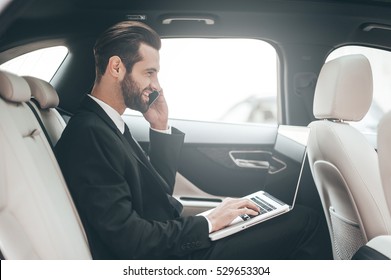 Time to make decision. Confident young businessman working on his laptop and talking on the phone while sitting in the car