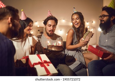 Time to make a wish. Young millennial birthday man makes a wish and blows out the candles on the cake surrounded by his friends. Holiday party. Birthday celebration concept at home.