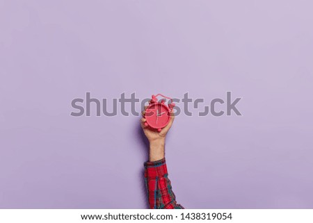 Time management, punctuality, awakening concept. Unrecognizable man holds little red alarm clock in hand, shows how much time left, isolated on purple wall. Timekeeper with mechanical watch.