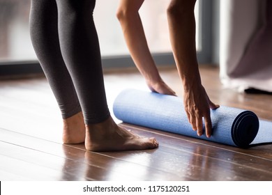 Time for meditation, fitness session, well-being concept. Girl wearing grey sporty pants rolling fitness mat before, after class in yoga studio club or at home on wooden floor. Hands and legs close up - Powered by Shutterstock