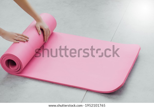 Time for meditation, fitness session, well-being\
concept. Girl wearing grey sporty pants rolling fitness mat before,\
after class in yoga studio club or at home on wooden floor. Hands\
and legs close up