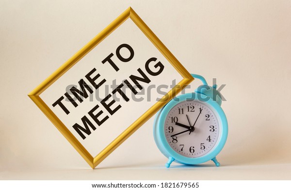 Time for a meeting, the\
text is written on a gold frame, next to an alarm clock on a white\
background