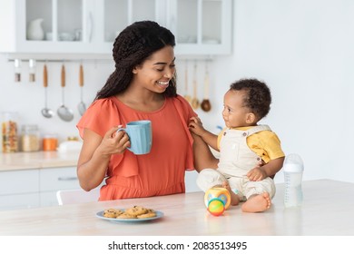 Time With Mom. Cute Little Black Baby Boy Relaxing With His Mother In Kitchen, Happy Young African American Mommy Drinking Coffee And Enjoying Playing With Her Adorable Infant Child At Home