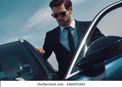 Time is money. Handsome young man entering his car while standing outdoors