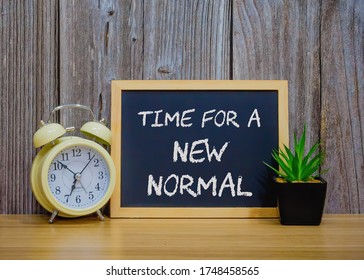 TIME FOR A NEW NORMAL text on wooden table with analog clock and flower pot. Life after covid-19 pandemic with social distancing and good hygiene