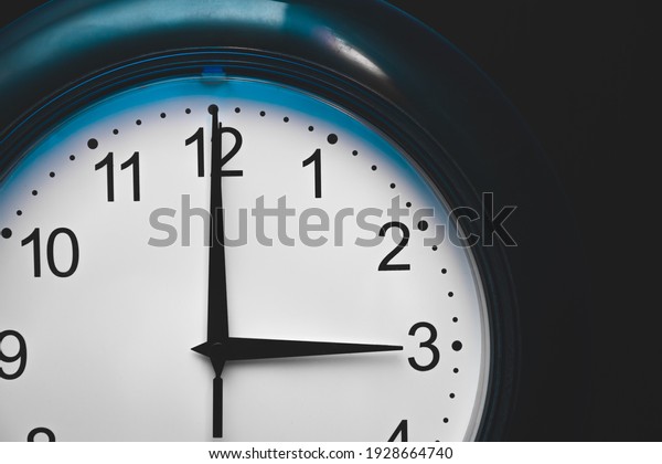 The time on the clock is\
three o\'clock, wall clock with blue frame, middle of the day or\
night.