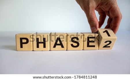 Time for Phase 2. Hand is turning a cube and changes the word 'Phase 1' to 'Phase 2'. Beautiful white background. Business concept. Copy space.