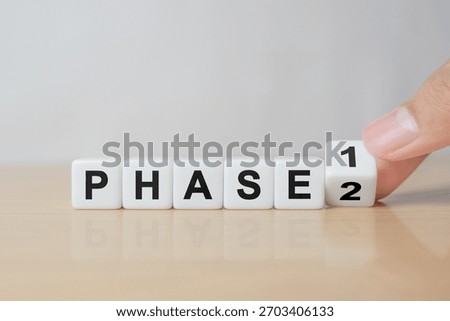 Time for Phase 2. Hand is turning a dice and changes the word 'Phase 1' to 'Phase 2'. Beautiful white background. Business concept