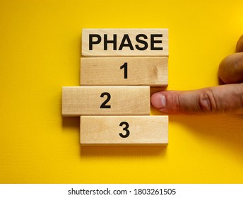Time to Phase 2. Wooden blocks form the words 'phase, 1, 2, 3,' on yellow background. Male hand. Beautiful background. Business concept.