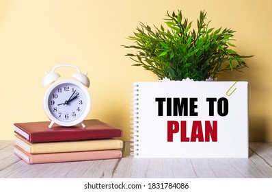 TIME TO PLAN is written in a notebook next to a green plant and a white alarm clock, which stands on colorful diaries. Organizational concept.