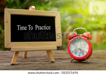 TIME TO PRACTICE! inscription written on chalkboard and red alarm clock on  old wooden desk . Time concept.