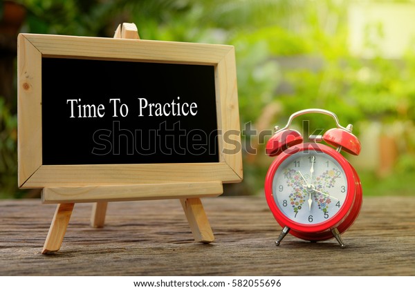 TIME TO PRACTICE!\
inscription written on chalkboard and red alarm clock on  old\
wooden desk . Time\
concept.