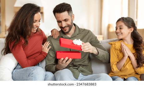 Time For Presents. Joyful Family Celebrating Holiday, Giving Gift Box To Father Sitting On Sofa At Home. Mom And Daughter Congratulating And Surprising Dad On His Birthday, Panorama - Powered by Shutterstock