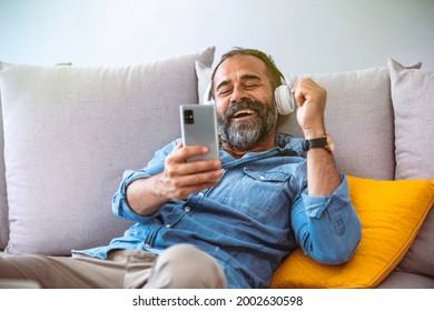 Time to relax. Joyful middle-aged bearded man in wireless headphones listening to music, copy space, closeup. Happy handsome man in headset with eyes closed relaxing on couch in living room