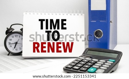 TIME TO RENEW words on white notebook and calculator, black vintage alarm clock and blue paper folder