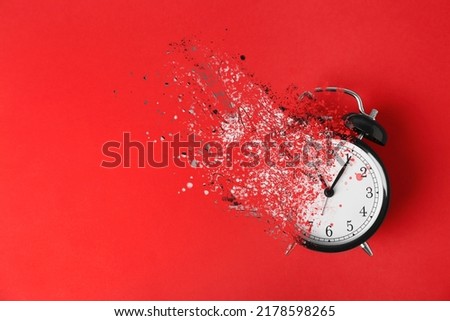 Time is running out. Black alarm clock vanishing on red background, top view