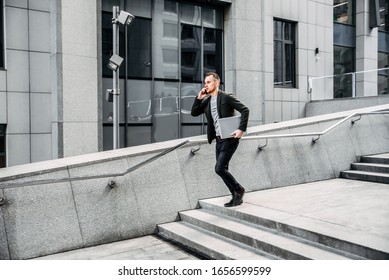 Time Is Running Out. A Young Man In Chic Casual Clothes Runs Up The Stairs To The Business Center Of The City. He Is Talking On The Phone, In His Hands Is A Laptop.