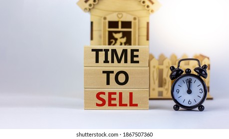 Time to sell real estate. Wooden blocks form the words 'time to sell' near miniature house. Black alarm clock. Beautiful white background. Business concept. Copy space.