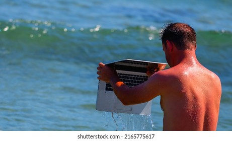 Time to take good care of your laptop computer. Funny humorous image of man on summer vacation by the sea washes his laptop in the water. Ð¡opy space.
