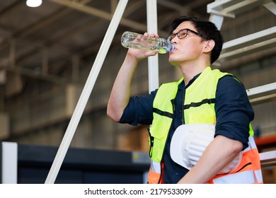 Time For A Tea Break Concept. Asian Male Warehouse Industrial, Factory And Energy Engineer Specialist Drinking Water Sitting On Stair At Warehouse Office Factory Workplace.