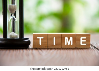 Time Text On Wooden Blocks With Minute Glass And Blurred Nature Background. Time Concept.