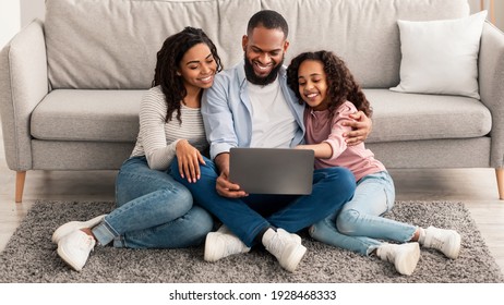 Time Together. Portrait of happy black family of three people using laptop computer together a home, watching movie, surfing internet or making video call sitting on the floor in living room