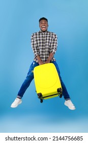 Time To Travel. Full Length Of Excited Young Black Man Jumping With Bright Suitcase Over Blue Studio Background. Happy Tourist Guy Ready For Summer Vacation Trip. Hot Tours Concept