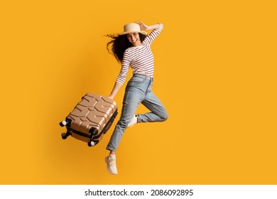 Time To Travel. Full Length Shot Of Cheerful Excited Young Woman Wearing Wicker Hat Jumping With Suitcase Over Yellow Background, Happy Tourist Lady Ready For Summer Vacation Trip, Copy Space