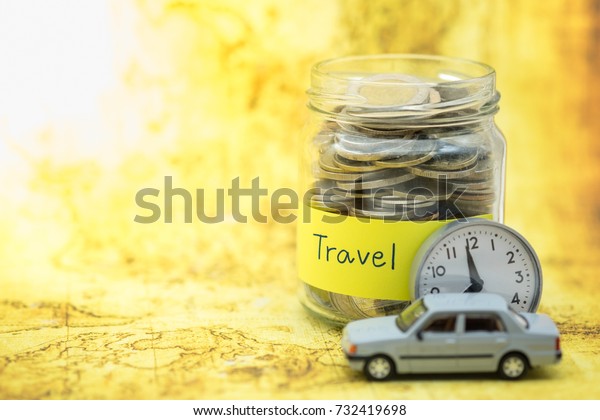 Time, Travel\
and Saving Concept. Full of coins in clear bottle with yellow label\
note with Travel word and mini car model and vintage round watch\
with world map as\
background.