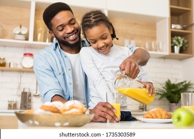 Time for vitamin C. Cute little african girl pouring fresh orange juice for her smiling daddy, spending time together at kitchen, copy space - Powered by Shutterstock