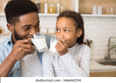 Time for vitamins. Cute Little Afro Girl And Her Handsome Dad Drinking Milk In Kitchen, watching each other