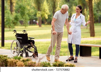 Time to walk in the park. A young female doctor helps the patient to walk on crutches, leaving his wheelchair behind. - Powered by Shutterstock