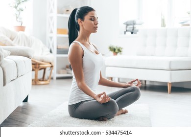 Time for yoga. Attractive young woman exercising and sitting in yoga lotus position while resting at home