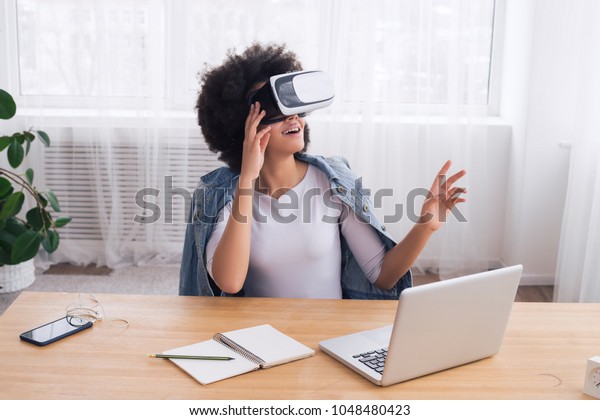 Time for yourself! Smart smiling young woman\
sitting beside her desk and having a great time, while using the\
virtual vision glasses.