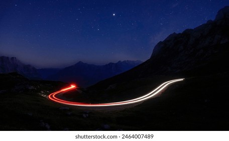 TIMELAPSE: Car lights create a blurry trail leading through the peaceful mountains at night. Cars driving up and down the mountain road under the starry sky. Tourists on road trip across Julian Alps