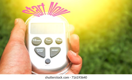 Timer in hand and wording Start Now on green lawn. Starting point concept