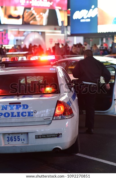 Times Square, New York, United States -\
February 20, 2018: Male police officer from NYPD getting into cop\
car with sirens on in New York City at\
night.